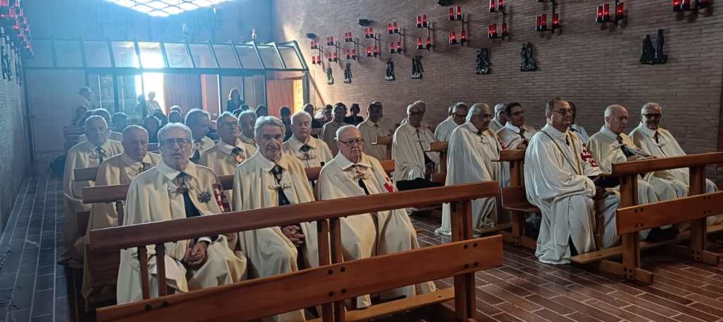 Un gruppo di uomini in abiti religiosi seduti su panche in una chiesa, durante un evento di preghiera.