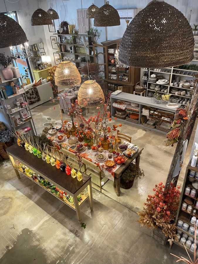 Interno del negozio 'Pan di Zucchero' con un grande tavolo decorato, esposizione di oggetti d'arredo e decorazioni floreali, lampadari sospesi in un ambiente accogliente e rinnovato.