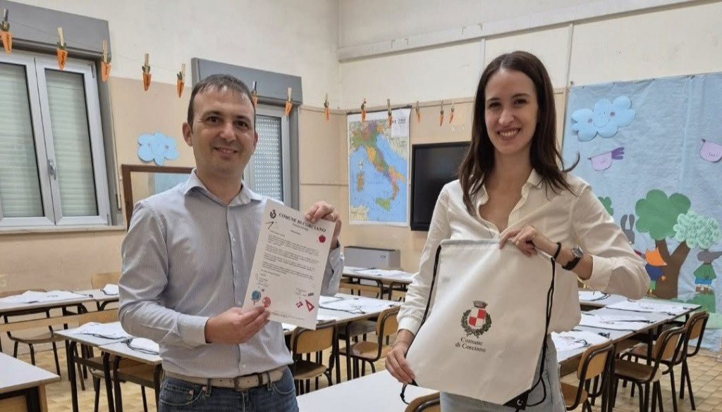 Il sindaco Lorenzo Pierotti e il vicesindaco Sara Motti in una aula scolastica, presentano un documento e un sacchetto con il simbolo del Comune di Corciano.