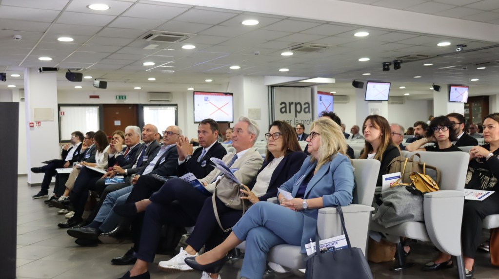 Un gruppo di esperti e professionisti partecipa a un convegno sulla endocardite infettiva, seduti in una sala auditorium con presentazioni visibili sullo sfondo.