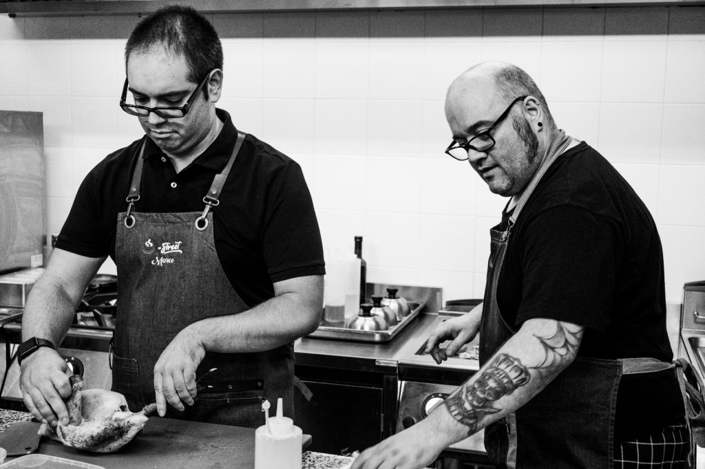 Due chef al lavoro in cucina, intenti nella preparazione di piatti in un ambiente ristorante moderno.