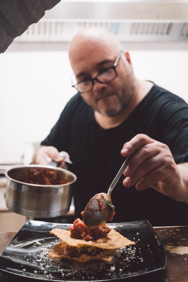 Un chef che prepara un piatto gourmet, posizionando un guazzetto su una base croccante in un ristorante moderno.
