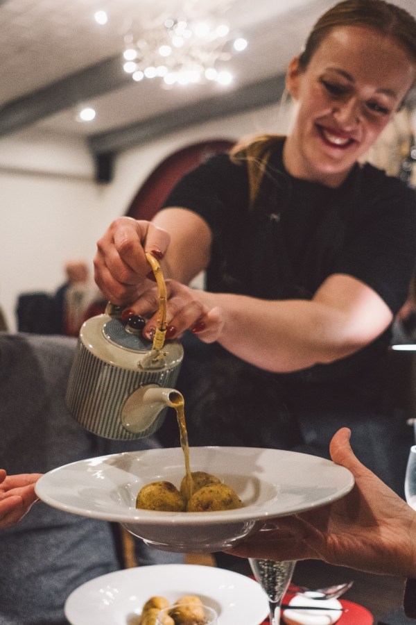 Una cameriera versa del brodo da una teiera su un piatto con gnocchi in un ristorante moderno.