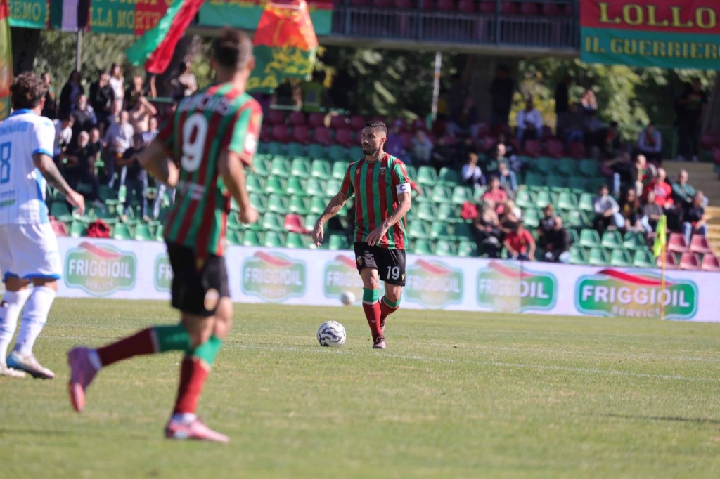 Un giocatore della Ternana con la maglia numero 19 in azione durante una partita di calcio, con tifosi e bandiere visibili nello sfondo.