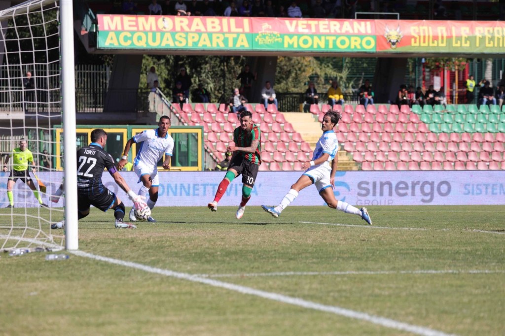 Giocatori di calcio in azione durante una partita, con il portiere avversario in porta e un attaccante della squadra che sta per calciare il pallone verso la rete.