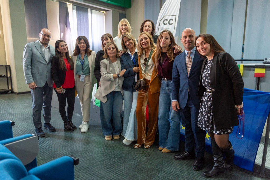 Gruppo di partecipanti alla cerimonia degli Erasmus Days, con rappresentanti della scuola e docenti, sorridenti e in un ambiente festoso, circondati da bandiere europee.