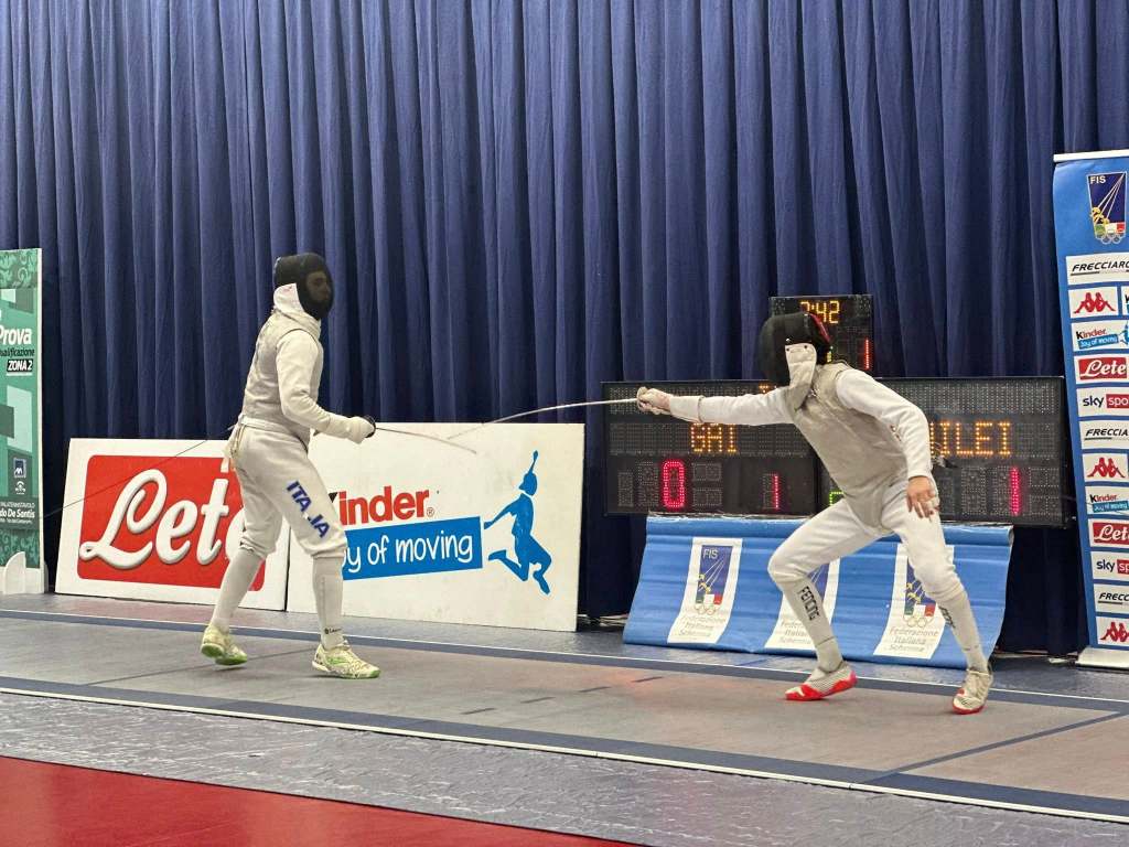 Due schermitori in competizione durante la 1ª Prova di Qualificazione Assoluti, nel Palatennistavolo di Terni, con una schermata che mostra il punteggio.