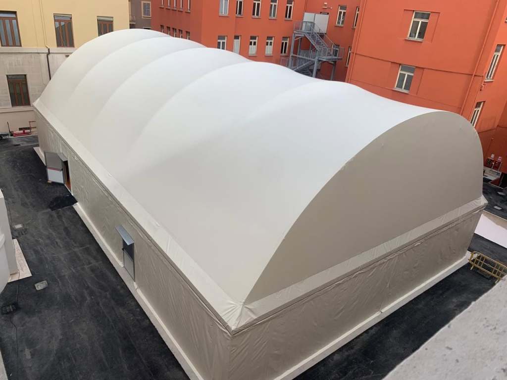 Immagine della palestra innovativa del liceo Classico Tacito di Terni, con una struttura lignea coperta da un telo chiaro, situata in un cortile scolastico.