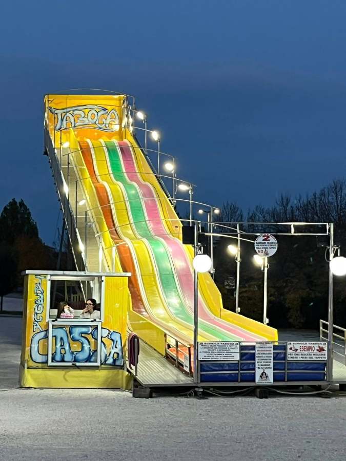 Scivolo colorato con diverse corsie al luna park, illuminato di sera, con postazione di controllo in primo piano.