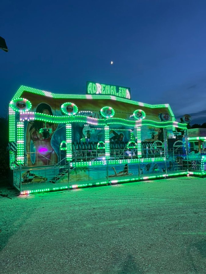 Una giostra illuminata di verde con il nome 'Adrenalina' visibile, allestita per un luna park al centro fiere di Montecastrilli, sullo sfondo del cielo serale.