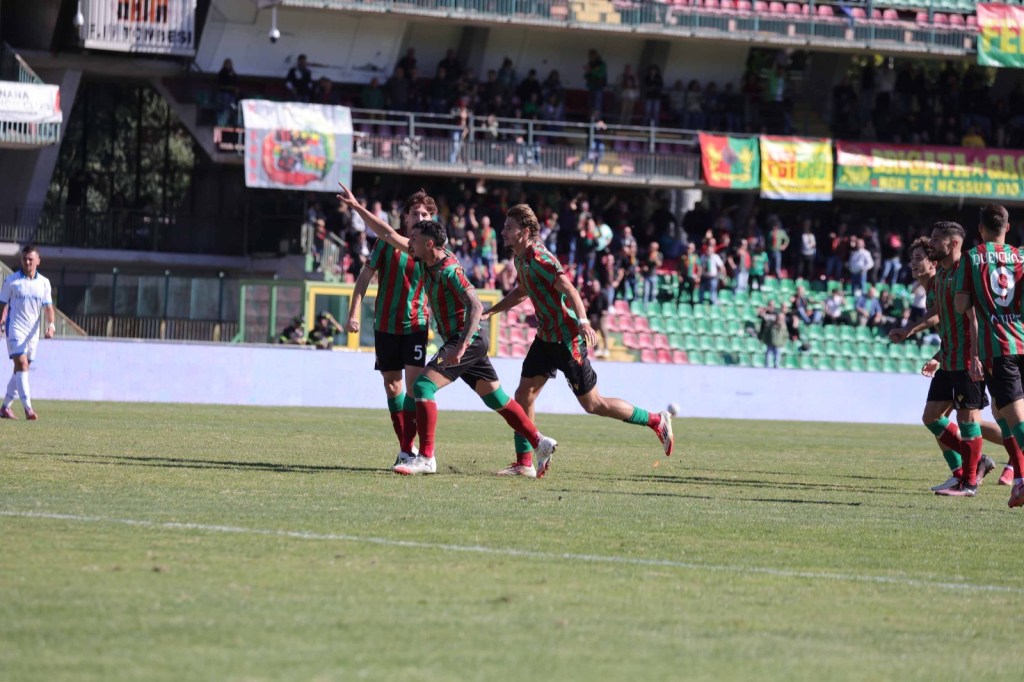 Giocatori della Ternana esultano dopo un gol durante una partita, con tifosi e bandiere sullo sfondo.