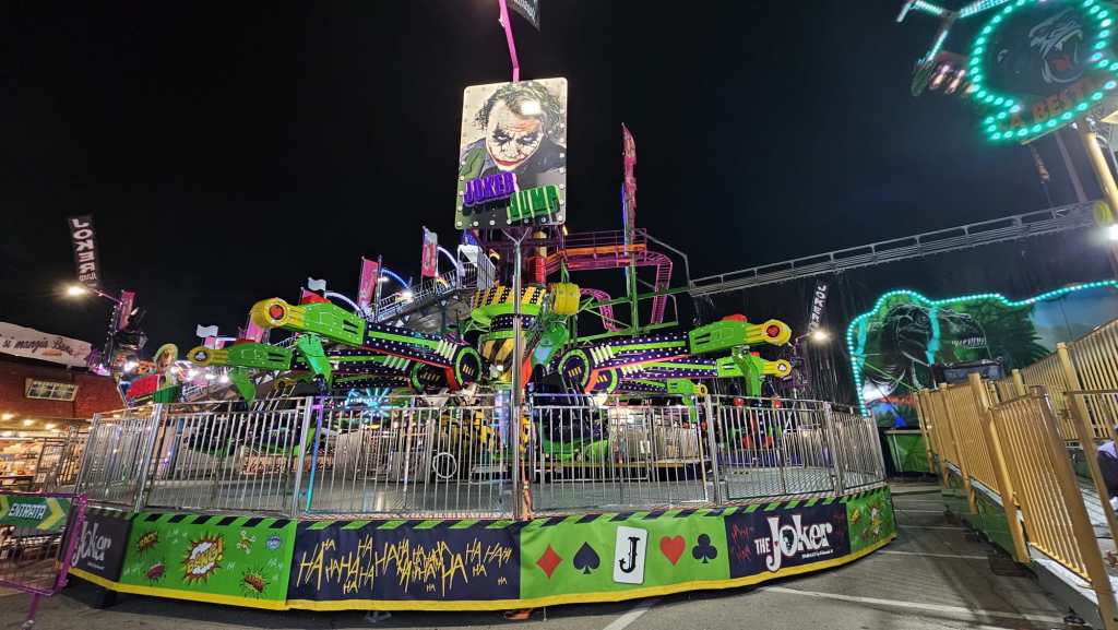 Attrazione del luna park 'The Joker' con luci colorate e decorazioni a tema, in un ambiente festivo notturno.