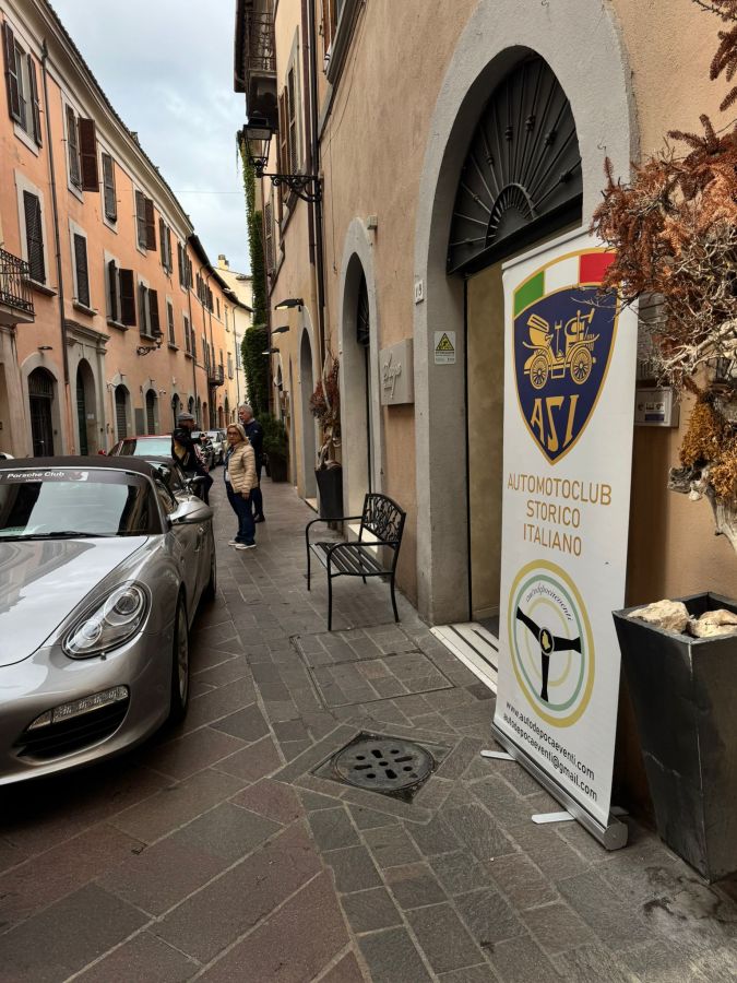 Un'auto sportiva parcheggiata lungo una via storica, con un'insegna dell'Automotoclub Storico Italiano accanto.