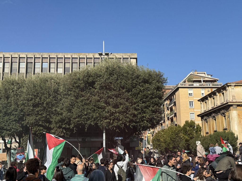 Un gruppo di manifestanti in piazza a Terni sventola bandiere palestinesi durante una protesta per sostenere la Palestina. Sullo sfondo, edifici e alberi sotto un cielo blu.