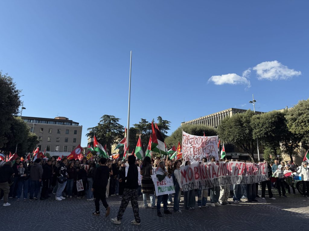 Manifestazione con moltissime persone in piazza che brandiscono striscioni e bandiere, protestando per la Palestina e contro il genocidio, in un'atmosfera di unità e determinazione.
