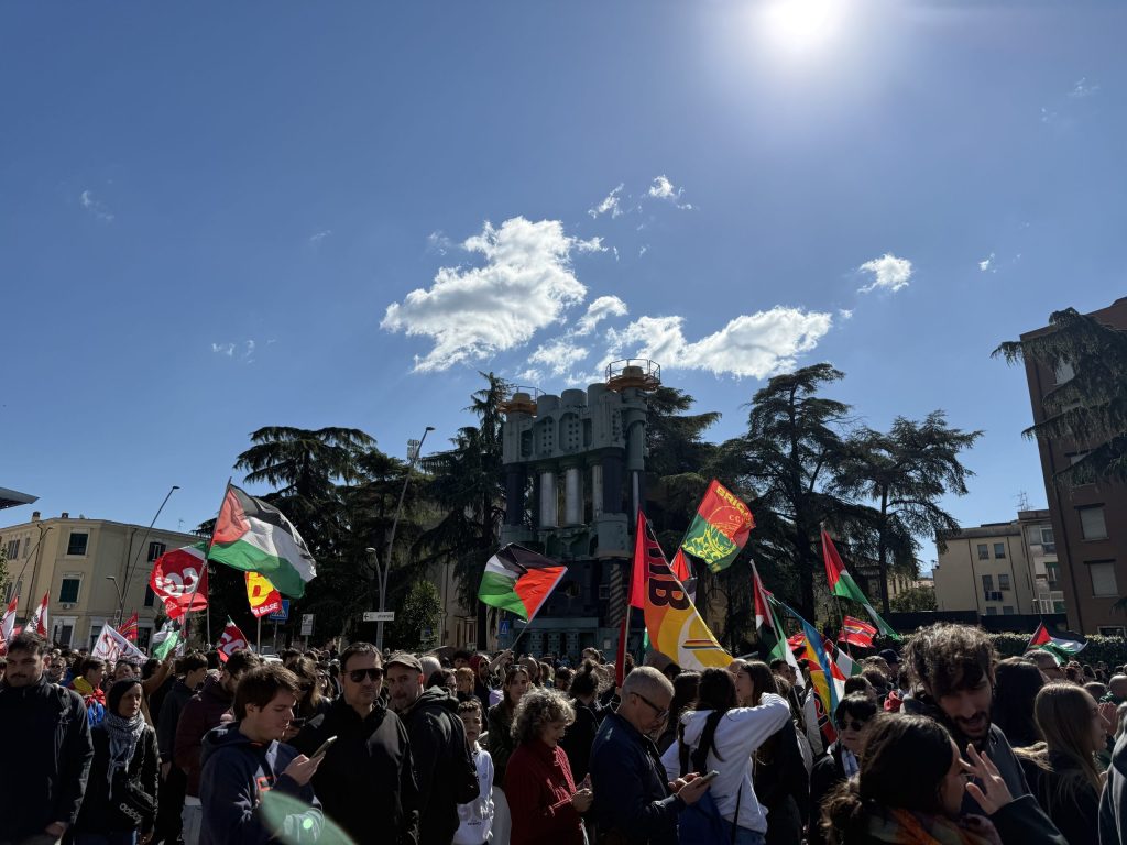 Migliaia di persone partecipano a una manifestazione per la Palestina, portando bandiere e striscioni, sotto un cielo sereno con qualche nuvola.