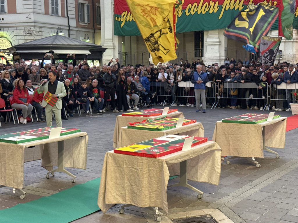 Evento di festa in piazza della Repubblica con la Ternana, con un presentatore e tavoli decorati, mentre la folla assiste e bandiere storiche volano in alto.