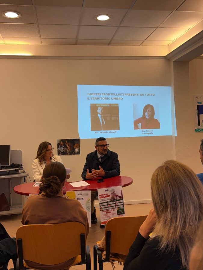 Un incontro durante l'inaugurazione dello sportello ADIC a Terni, con relatori seduti a un tavolo mentre il pubblico ascolta. Sullo sfondo, presentazioni dei relatori.