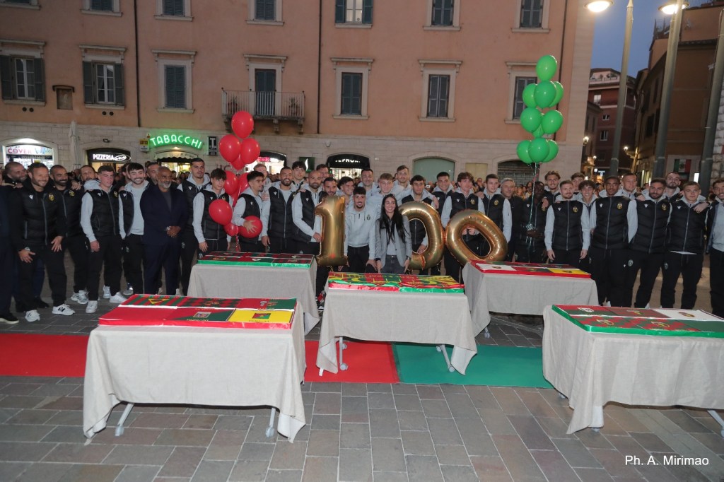 Il team della Ternana posizionato in piazza con palloni rossi e verdi, mentre celebrano un evento con torte colorate e decorazioni festive.