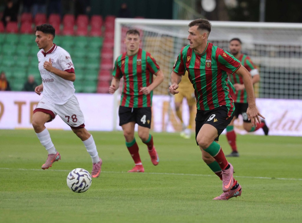 Due calciatori in campo durante una partita di calcio, con il giocatore in divisa rossa e verde che si prepara a ricevere il pallone.
