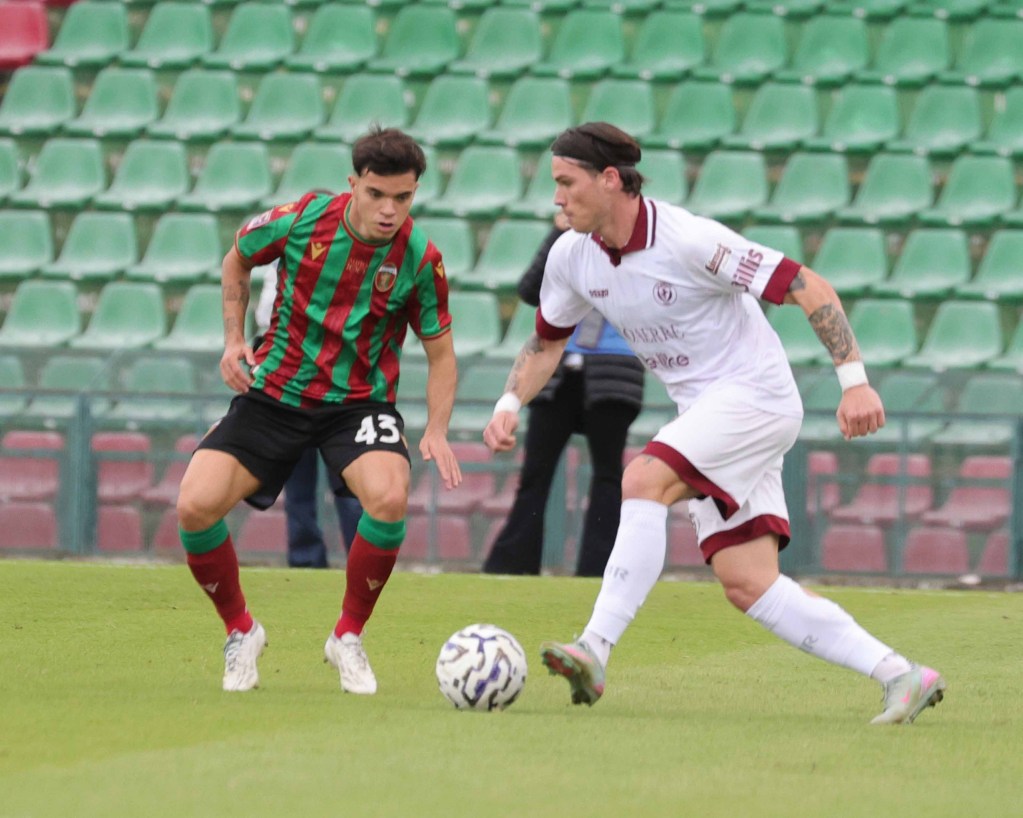 Due calciatori in azione durante una partita di calcio, sul campo con seggiolini verdi sullo sfondo.