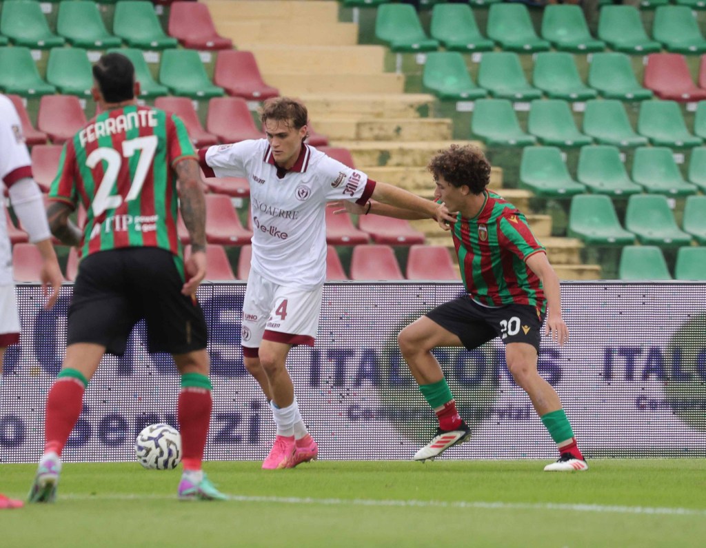 Giocatori di calcio in azione durante una partita, uno indossa una maglia bianca con il numero 4 e l'altro una maglia a strisce verdi e rosse con il numero 20.