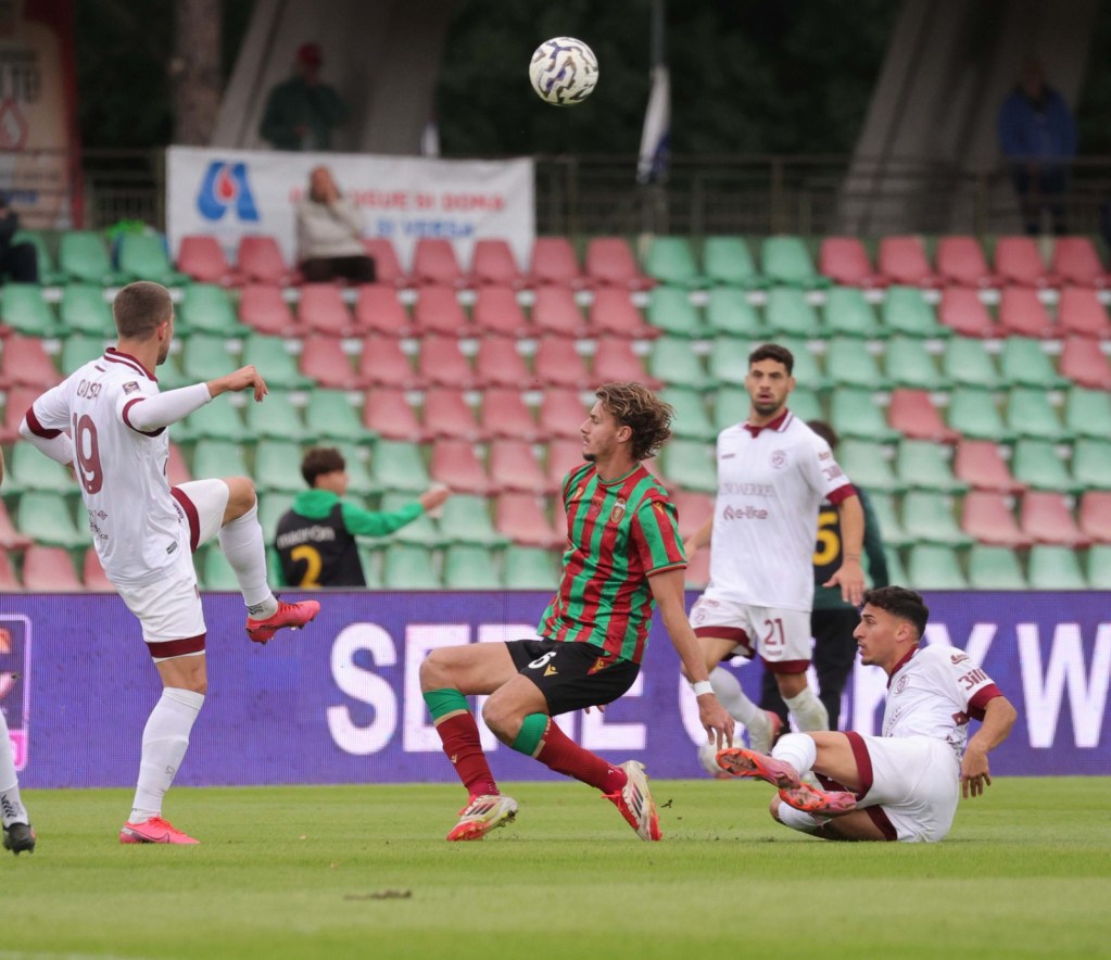 Giocatori di calcio durante un'azione di gioco, con un atleta della Ternana in maglia a strisce verde e rosse che cerca di controllare la palla mentre gli avversari si preparano a intervenire.