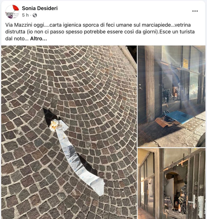 A close-up view of dirty toilet paper lying on a cobblestone sidewalk, with a background of a damaged storefront and debris scattered on the floor.