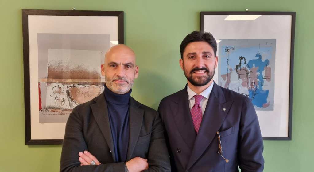 Luca Secondi, newly elected president of Federsanità Anci Umbria, poses alongside Emanuele Ciotti, the newly appointed vice president, in front of framed abstract artworks on a green wall.