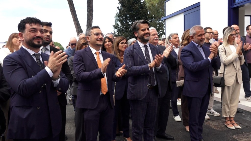Un gruppo di persone applaude durante l'inaugurazione del Vita Hub di Vitakraft a Castiglione del Lago, con alcuni individui in abiti formali e sorridenti nel pubblico.
