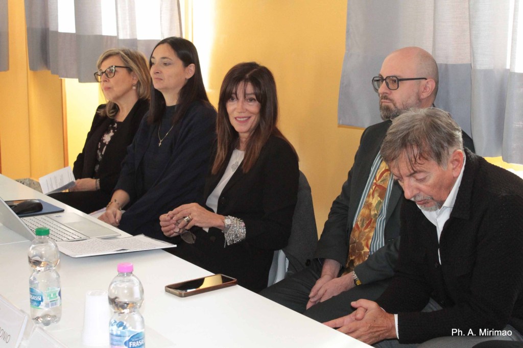 A panel of five professionals seated at a table during a discussion in a brightly lit room with yellow walls.