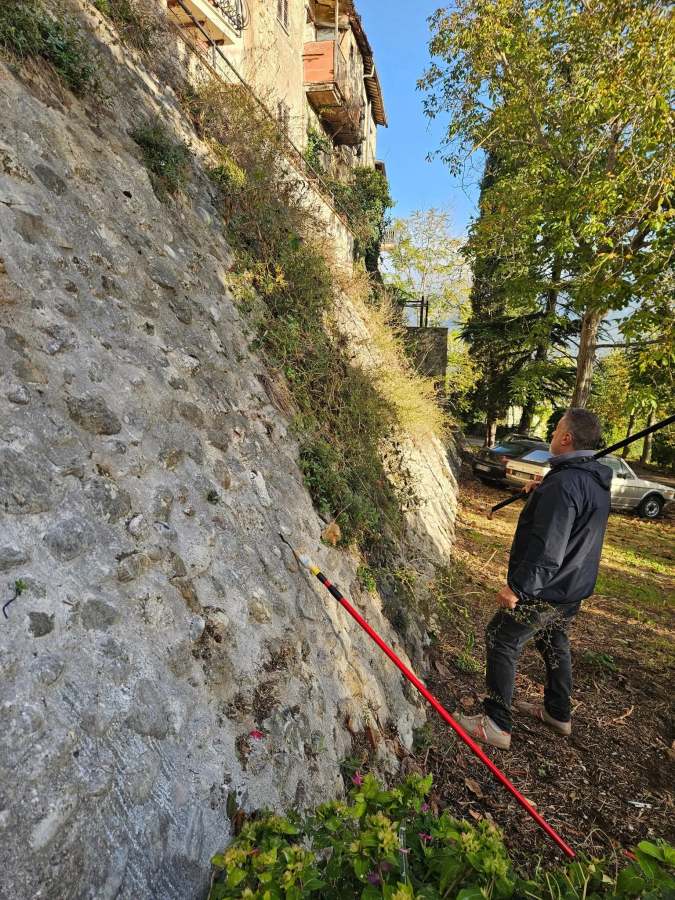 Un volontario osserva le antiche mura di Collescipoli mentre rimuove erbacce e rifiuti, contribuendo al restauro del patrimonio storico.