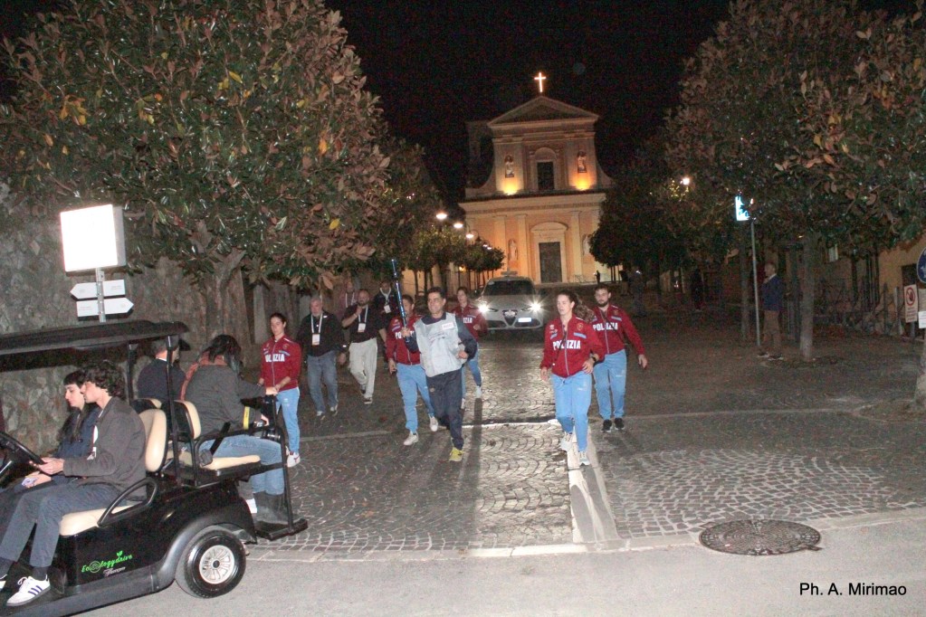 A group of people wearing POLIZIA jackets walking down a cobblestone street at night, with a church in the background.