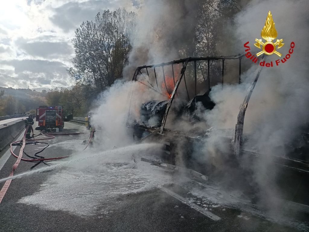 Intervento dei vigili del fuoco per spegnere un incendio di un autotreno in fiamme sulla strada statale 76 a Gubbio, con fumi e acqua che escono mentre si procede all'estinzione.