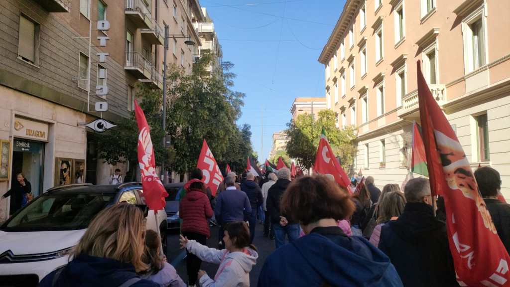 Un gruppo di persone partecipa a una manifestazione per la Palestina, sventolando bandiere rosse e della Palestina lungo una strada di Terni.
