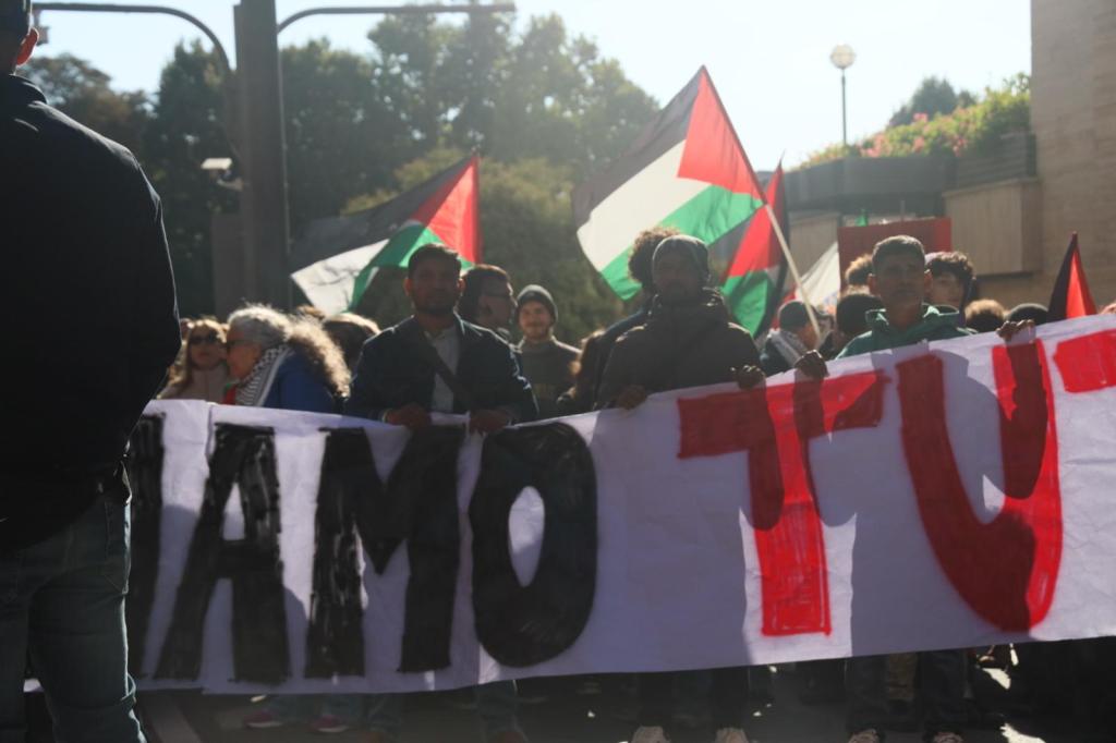 Manifestanti in una marcia per la pace, con bandiere palestinesi e uno striscione che recita 'SIAMO TUTTI'.