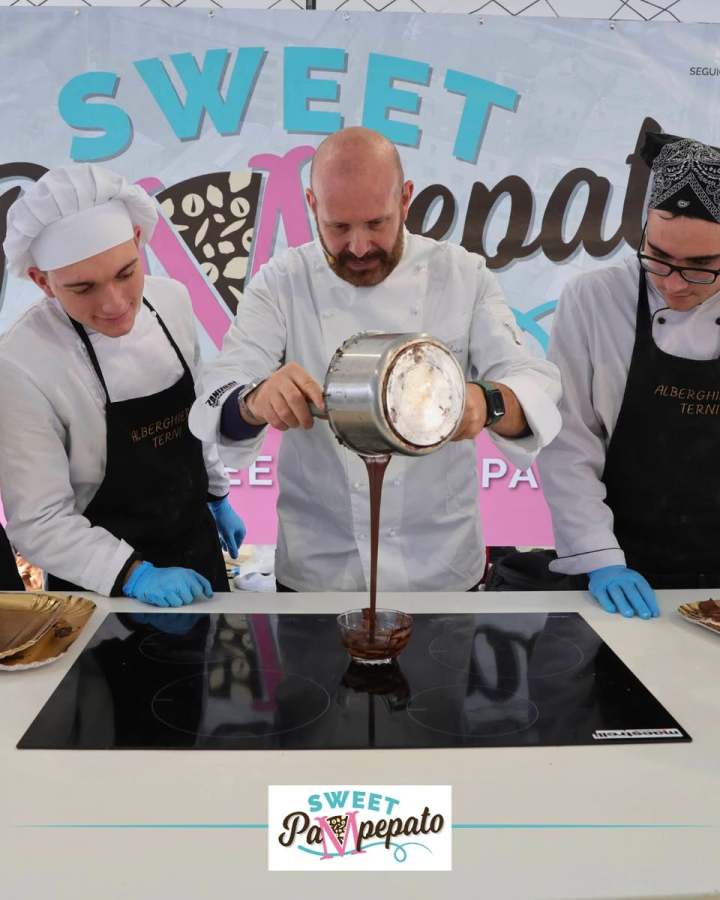 Chef pouring chocolate during a cooking demonstration at the Sweet Pampepato festival in Terni, with assistants by his side.