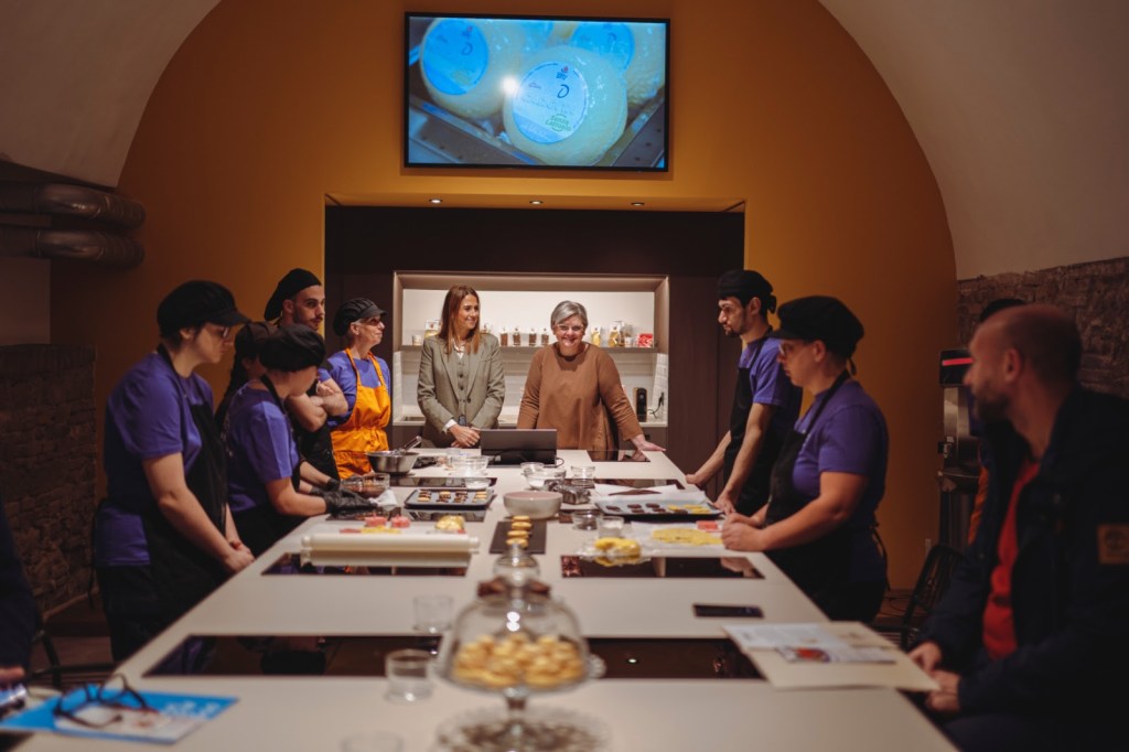Un gruppo di giovani lavoratori di La Brigata Indipendente si riunisce attorno a un tavolo nel LAB - Luisa Annibale Base, mentre presentano i loro prodotti da forno e pasticceria.
