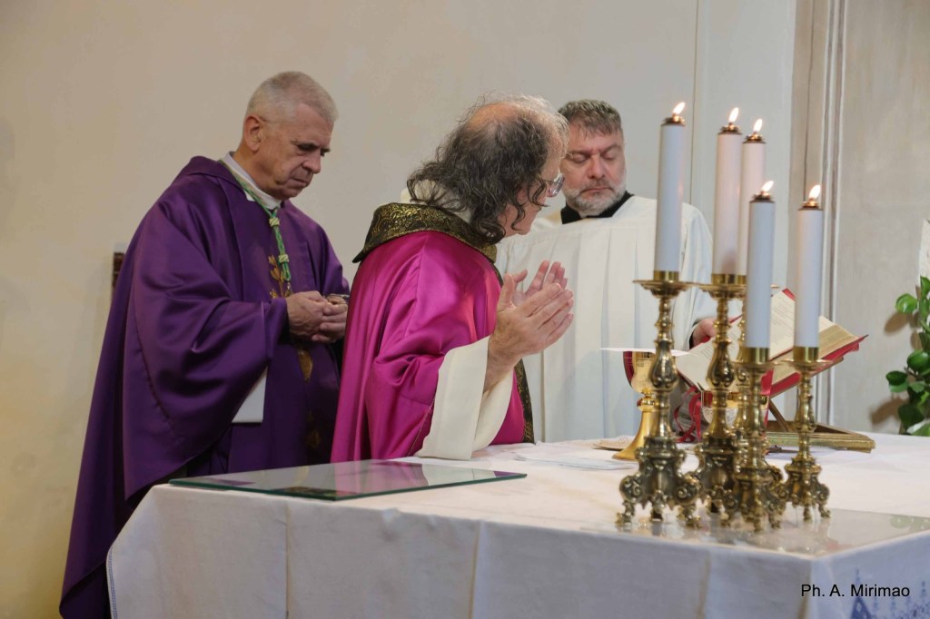 Three clergy members performing a religious ceremony at an altar, with candles lit and a book open on the table.