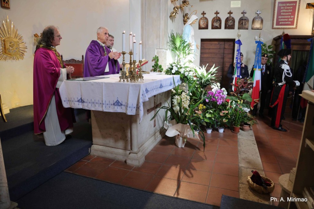 Three clergy members in purple vestments participate in a religious ceremony at an altar adorned with flowers, candles, and religious artifacts in a small church setting.