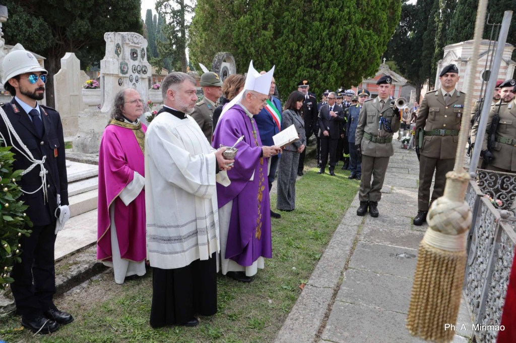 Ceremony at a cemetery with clergy and military personnel, including a priest in purple robes, during a memorial service.