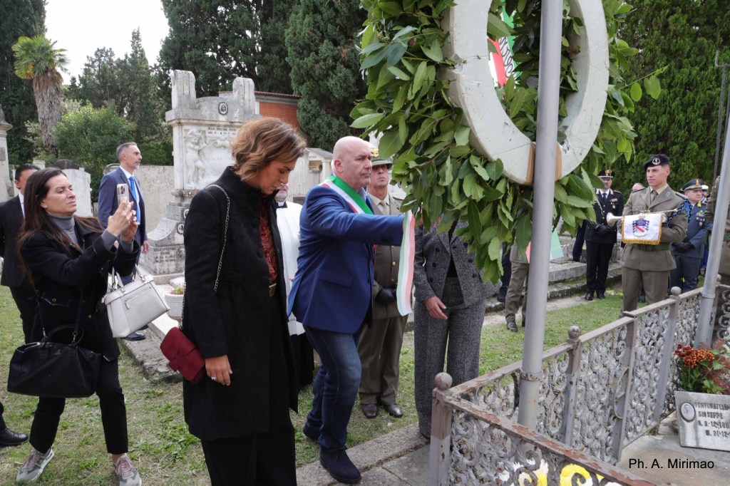 A group of people gathered at a cemetery, with one person laying a wreath while others observe the ceremony.