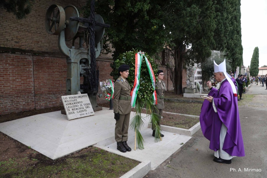 Ceremony honoring fallen soldiers, featuring military personnel saluting and a cleric performing a blessing beside a memorial.