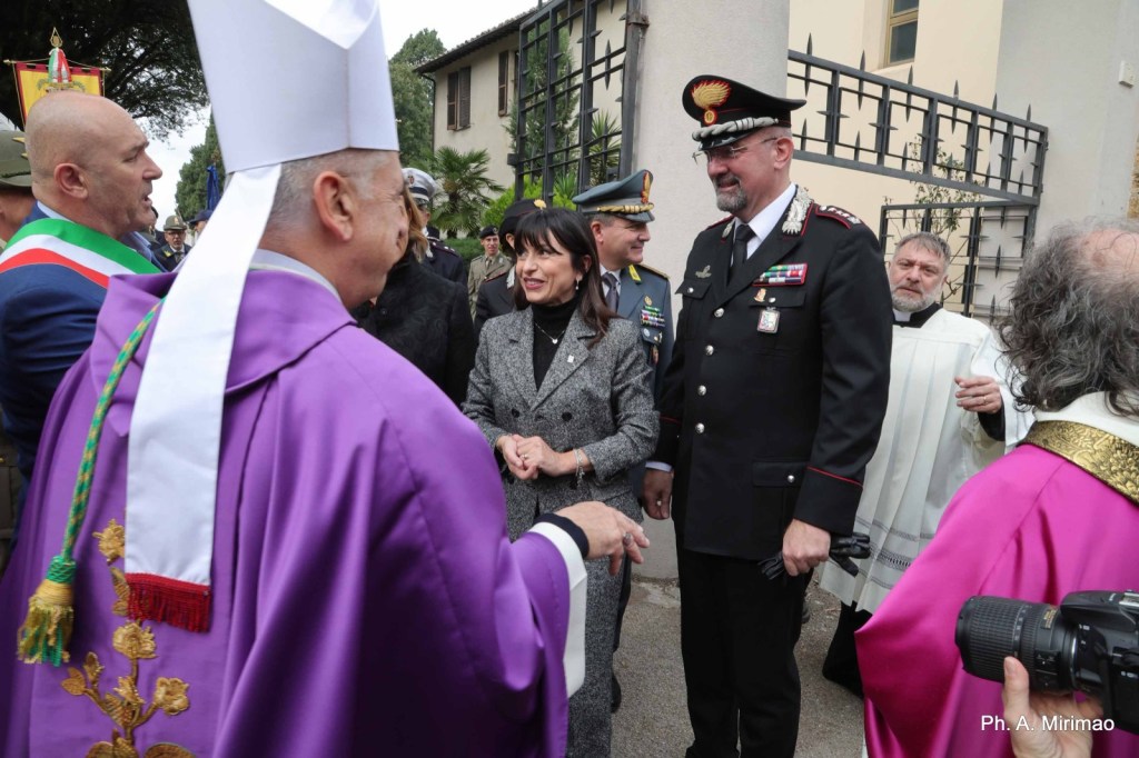 A group of individuals, including a man in a purple robe and others in military and formal attire, engage in conversation outdoors during a formal event.