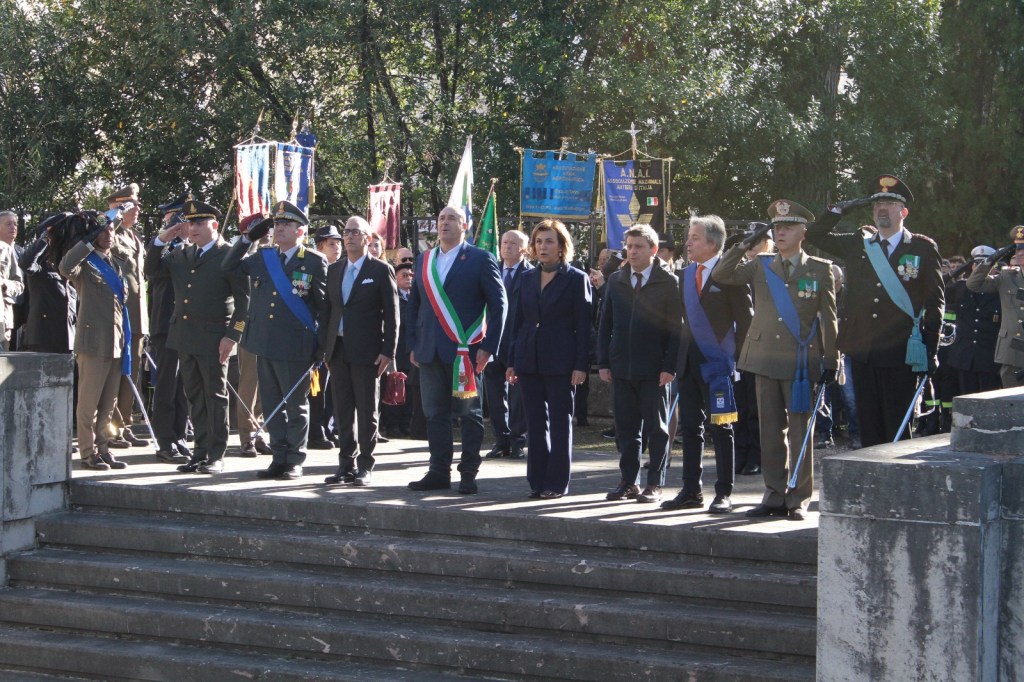 Ceremony with military and government officials standing at attention, saluting, and commemorating an event outdoors, with banners in the background.