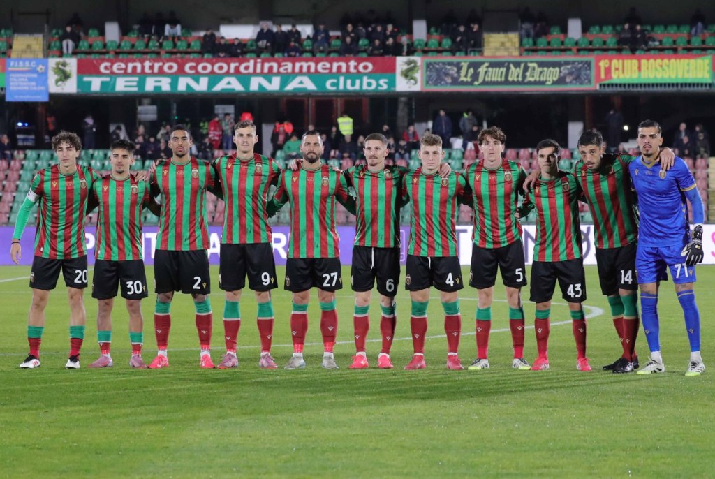 La squadra Ternana schierata sul campo, indossando maglie a strisce verdi e rosse, con elementi in fila e sorridenti, prima dell'inizio della partita.
