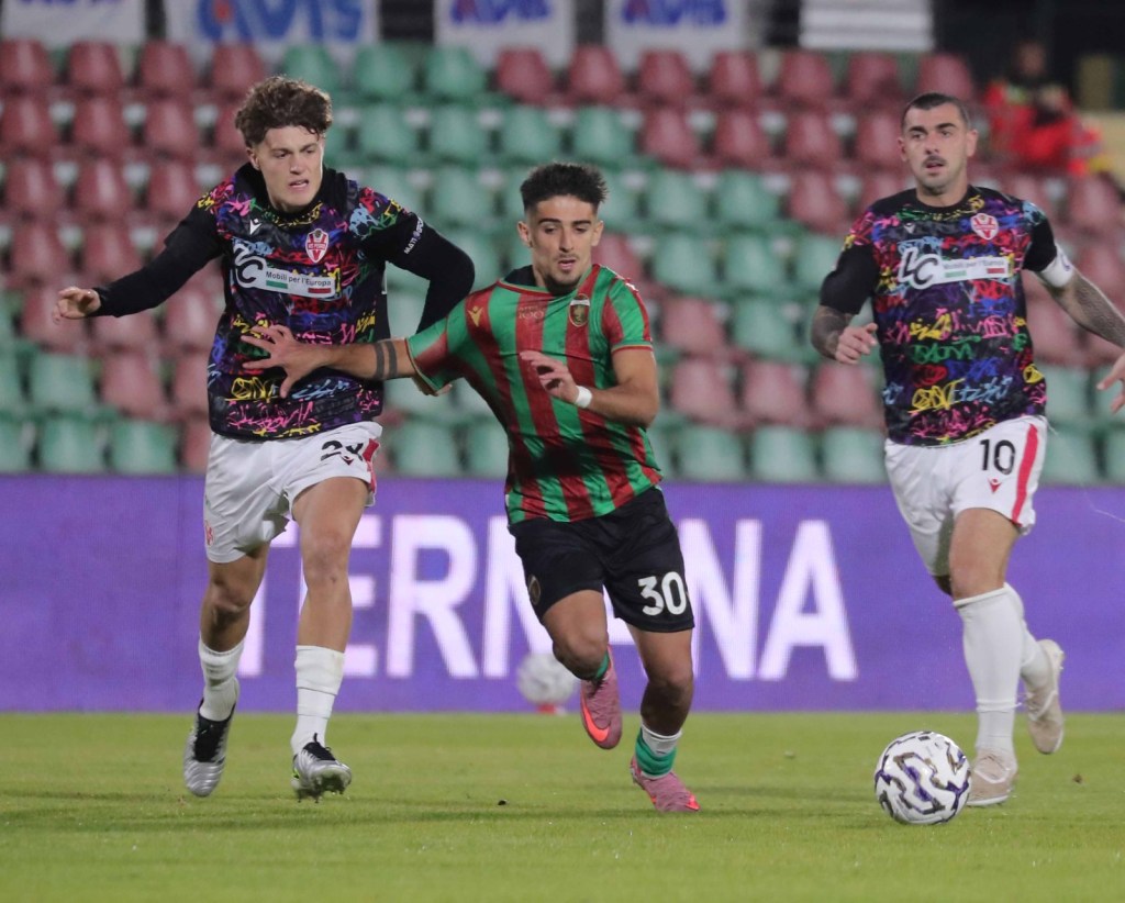 Due giocatori avversari in fase di inseguimento mentre un terzo gioca con il pallone, durante una partita di calcio.