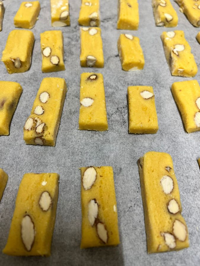 Fette di biscotto giallo con mandorle, disposte su una teglia rivestita di carta da forno.