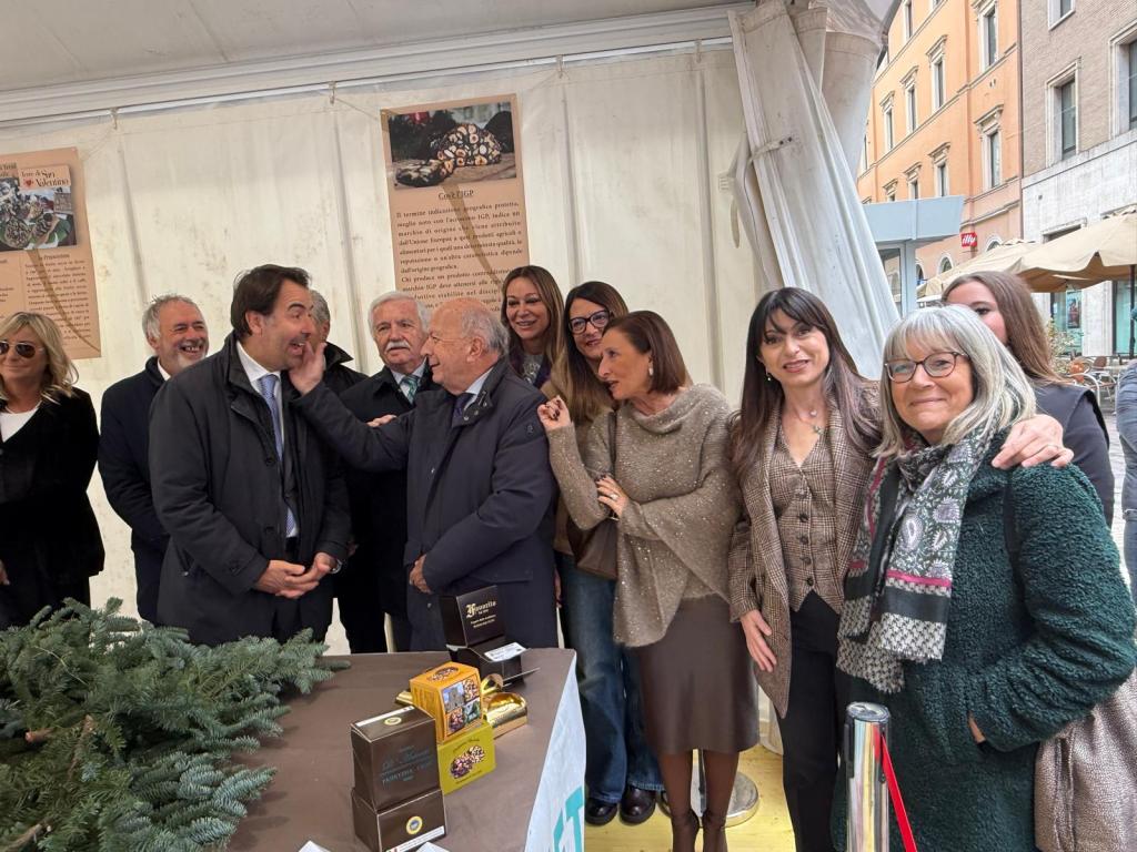 A group of people smiling and interacting at an event, with a decorated booth in the background and informational posters displayed.