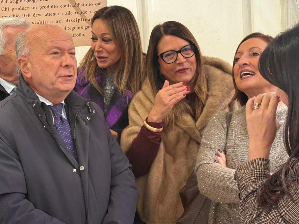 A group of four women and one man engaged in conversation, showcasing expressions of laughter and enjoyment in a social setting.